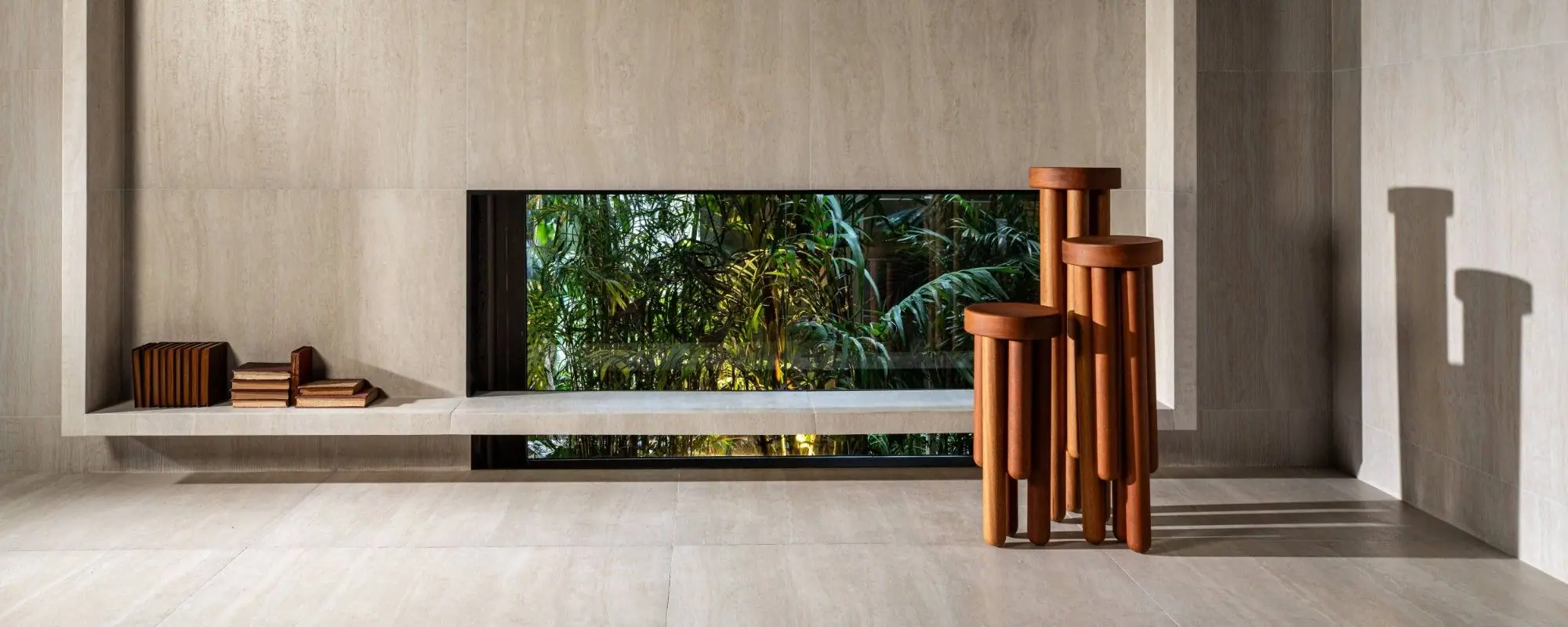 Ambiente com porcelanato efeito travertino bege em piso e parede, janela para o jardim e banquetas de madeira